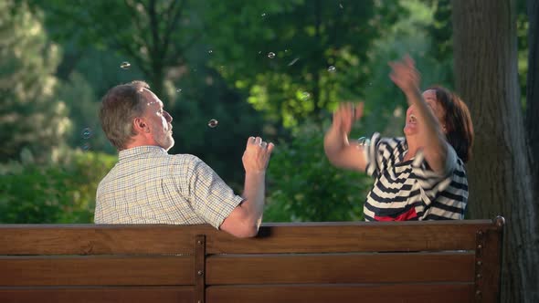 Senior Couple with Bubble Blower on Bench at Park