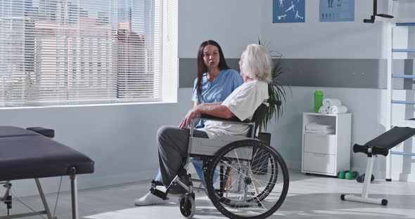 Friendly Rehabilitation Therapist Speaking with Handicapped Aged Patient