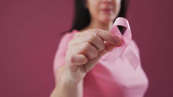 Mid section of woman holding a pink ribbon against pink background