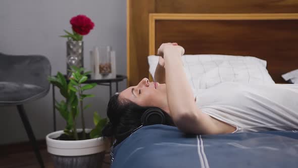 Woman Lying on Bed and Enjoying Modern Music in Headphones