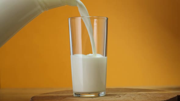 Close up Milk poured into glass from jar on wooden board with color background. Close up. HD