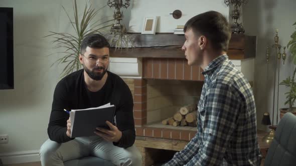 Male Caucasian Psychologist in Eyeglasses Holding Notes and Talking To His Sad Patient