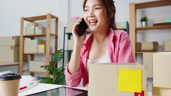 Young Asian woman using phone call receiving purchase order and check product on stock work at home.