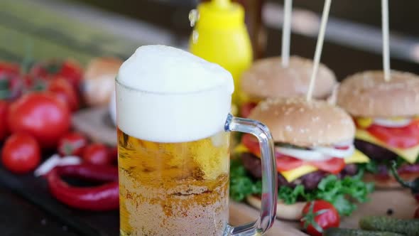 Pouring Beer Into Glass Mug with Cheeseburgers Served with French Fries on Background