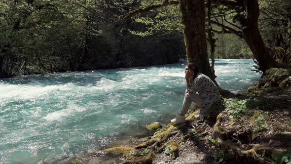 Young Woman Sits on the Shore Near the Swift River Stream She Looks at the Water