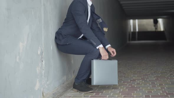 Side View of Desperate Businessman Sitting Down Leaned Against the Wall in Urban Underground