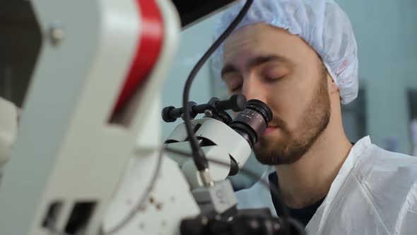 Young Doctor Using Loking at Eyepieces of Microscope Complex System in a Hospital Laboratory