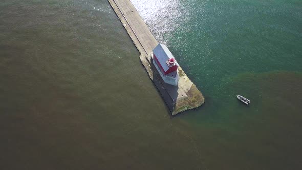 Aerial view of lighthouse/beacon on pier in Michigan, USA. Small boat beside it. Drone circles to th