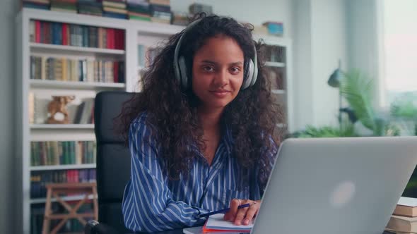 Young Indian Woman in Headset Looks Intently at Camera Sits at Office Table