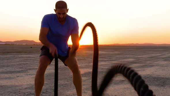 Athletic man working out with battle ropes on a dry lake at sunset