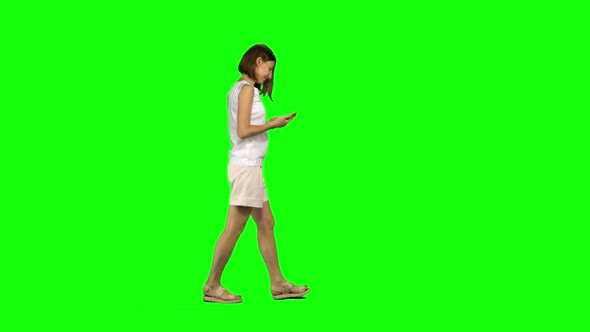 Young Woman Is Calmly Walking and Texting Message Vie Her Mobile Phone on Green Screen. Profile View