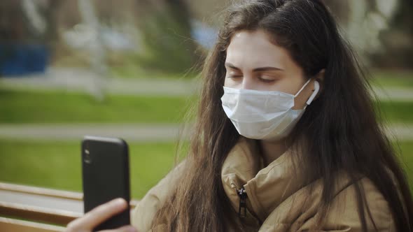 Young Woman in Protective Mask Using Smartphone for Video Calling or Recording Video in the City