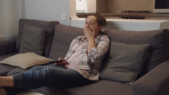 Moving Shot of Weary Adult Woman Yawning Watching TV Set at Home