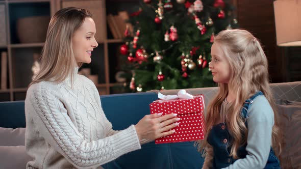 Happy Caring Mother Giving Festive Wrapped Gift Box to Cute Little Daughter Congratulations Xmas Eve