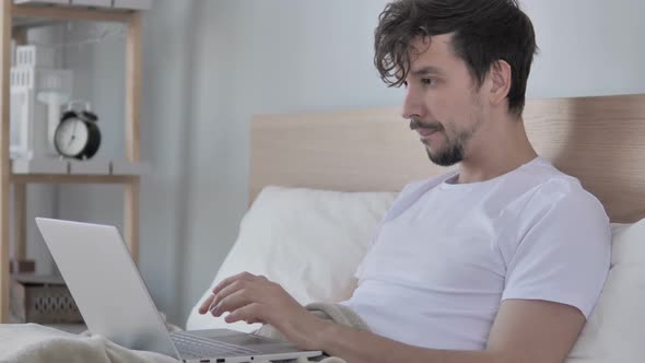 Sad Young Man Facing Loss While Using Laptop in Bed