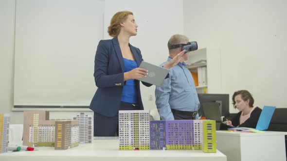 Woman with Tablet in Hands Shows Something To Colleague in Virtual Glasses in the Office