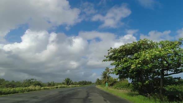 POV Driving Along Two Lane Road on Tropical Island Against Blue Sky and Clouds