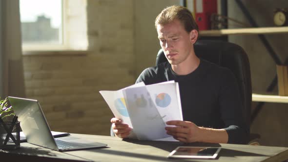 Handsome Concentrated Young Businessman Sitting at the Office Desk and Working with Documents