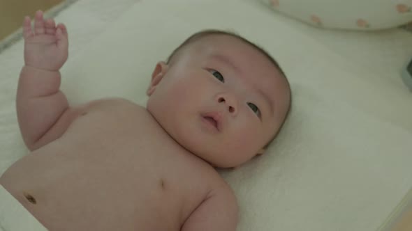 An East Asian newborn baby lying in bed and playing.