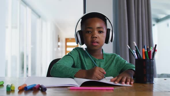 Portrait of african american boy waving and doing homework looking at the camera
