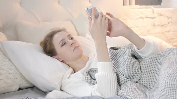 Young Woman Using Smartphone while lying in Bed