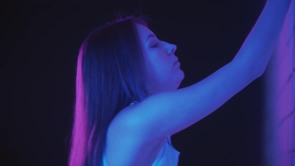 Young Woman Exercising in Neon Lighting Indoors Bends Her Back Leaning with Her Hands Against the