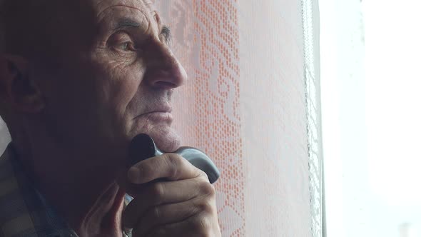 Portrait of a pensive caucasian pensioner 70 years old with a walking stick bored at the window.The 