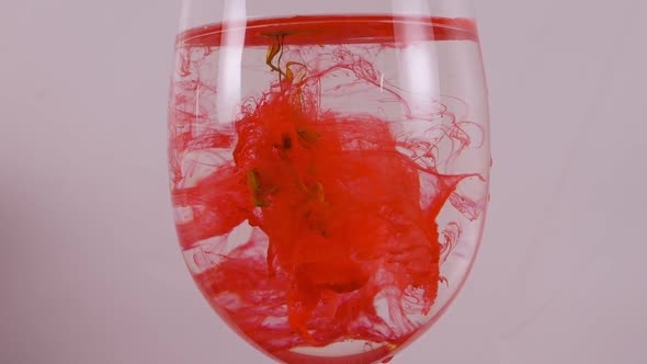 Red Ink Swirls in a Wine Glass Against a White Background