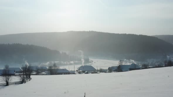 Aerial View of a Village with Wooden Houses on the Bank of a Frozen River in Winter