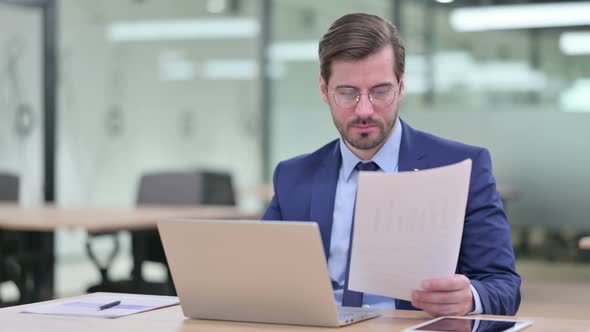 Serious Businessman Working on Laptop with Documents 