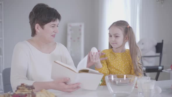 Cute Caucasian Little Girl Gathering Ingredients for Pancakes As Grandmother Reading the Recipe