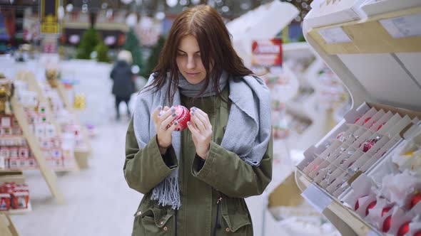 A Young Beautiful Woman Walks Around the Store and Selects Christmas Decorations and Decorations to