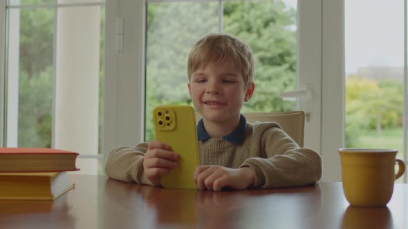 School Boy Using Mobile Phone Sitting at Home By the Window