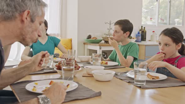 Three kids having breakfast of pancakes and fruits with their parents