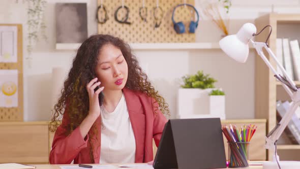 Business woman professional talking on phone using tablet sitting at home office desk, serious talk