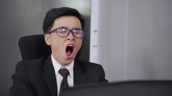 tired young businessman using laptop and yawning