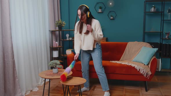 Young Dancing Woman Dusting Furniture Alone Caring for Hygiene Using Colorful Duster in Room at Home