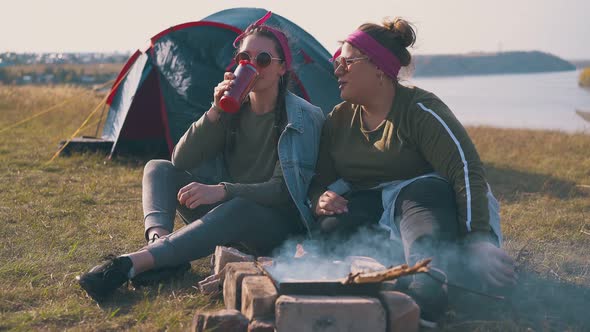 Happy Girls Drink Tea at Burning Bonfire Near Blue Tent