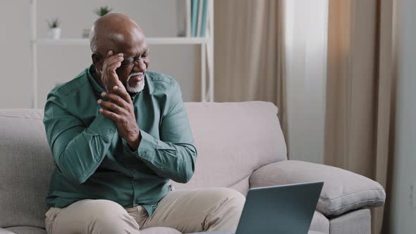 Old Bald African Business Man with Gray Beard Aged Male Employer Sitting on Sofa Working with Laptop