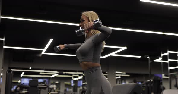 Fit Woman Doing Exercise with Dumbbells for Deltoids in the Gym