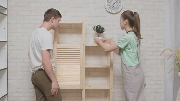 Happy couple woman and man rejoice at successful completion of assembly of wooden bookcase