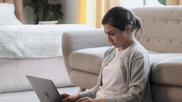 From above of thoughtful self employed woman sitting on floor in cozy apartment and working