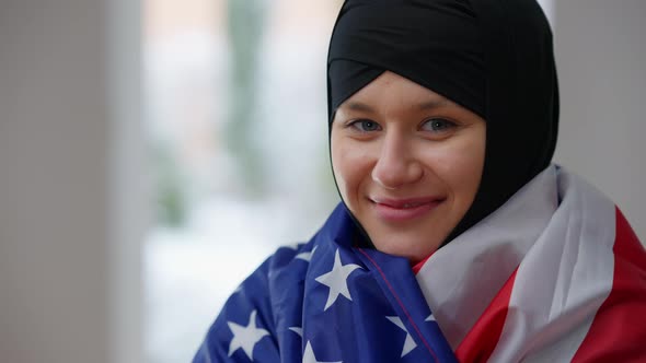 Closeup of Happy Muslim Woman in Hijab Wrapping in American Flag Smiling Looking at Camera