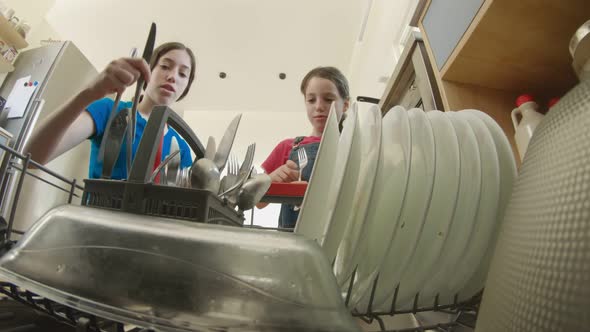 Two girls fill the dishwasher with dirty dishes