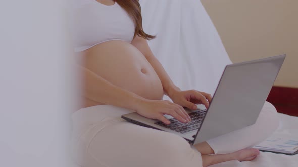 Pregnant business woman sitting and working on the laptop with sale report,tablet at home