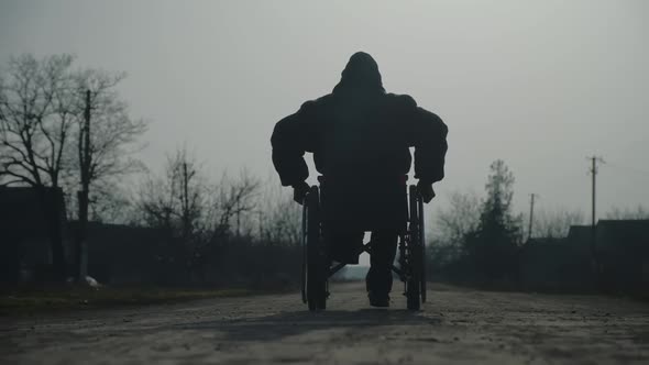 Amputee Man in Warm Jacket Rides Wheelchair on Ground Road