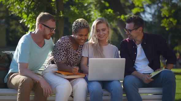 Multiethnic College Friends Relaxing After Classes Sitting Together On Bench Outdoors In Park