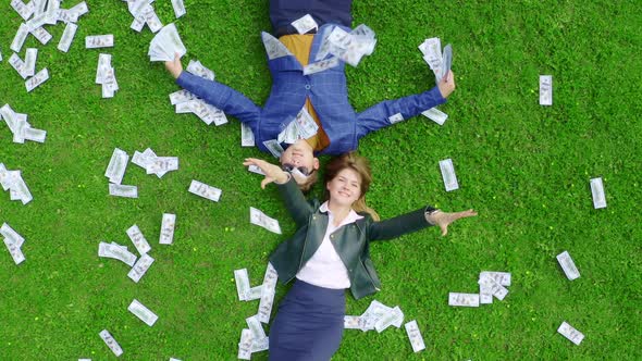 Young Beautiful and Successful Business Lady Lies on a Green Grassy Lawn Strewn with Money