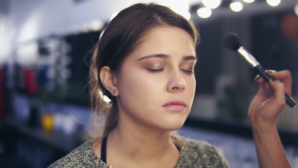 Closeup View of Professional Makeup Artist's Hands Applying Facial Powder on Young Woman's Skin