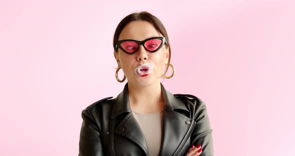 Portrait unusual stylish woman inflates bubble from chewing gum and bursts in pink sunglasses